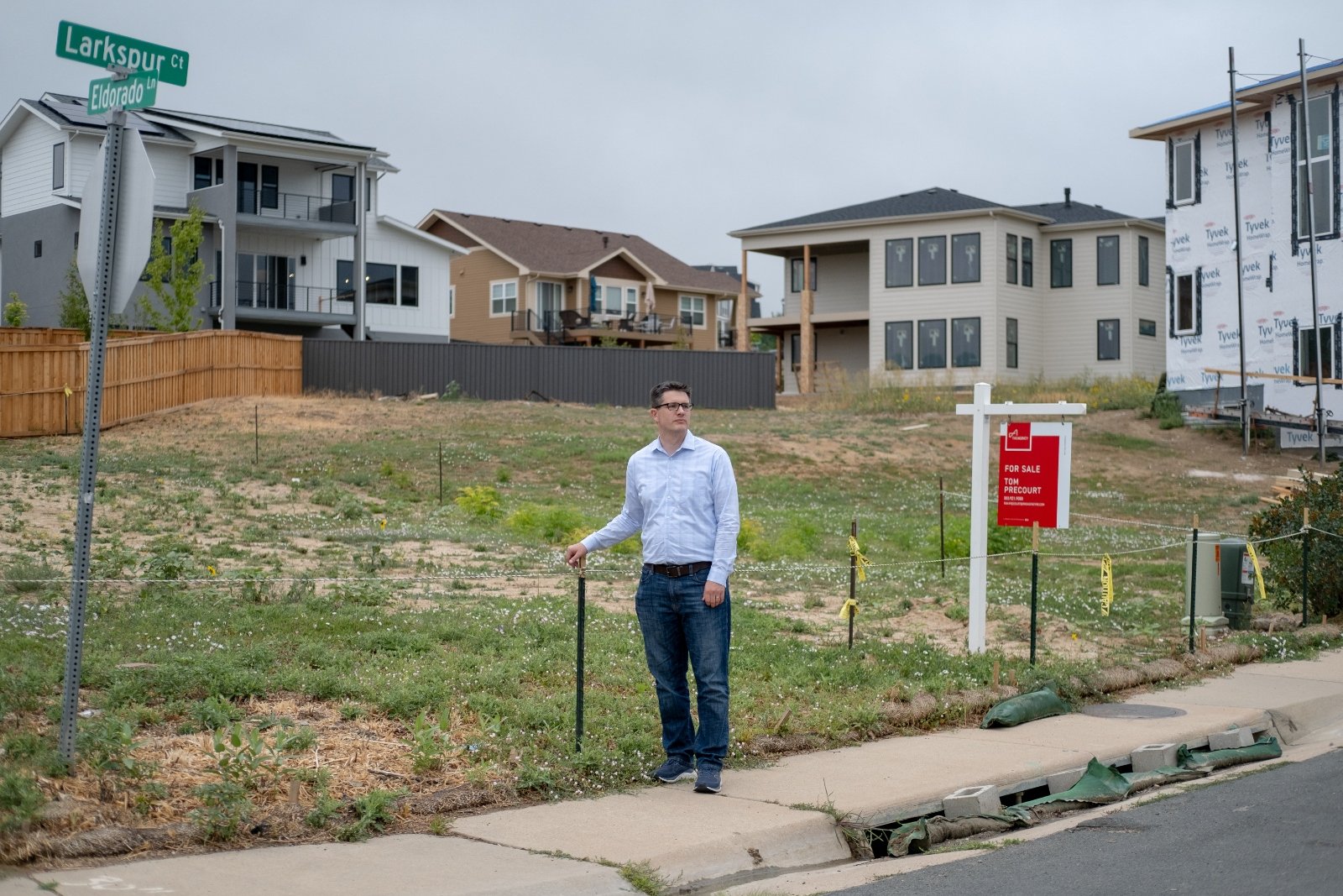 A man in jeans and a collared shirt stands among houses under construction